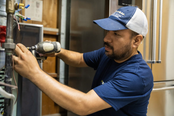 Triton plumbing and heating service technician repairing a residential HVAC system.