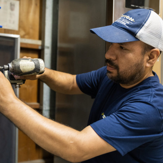 Triton plumbing and heating service technician repairing a residential HVAC system.